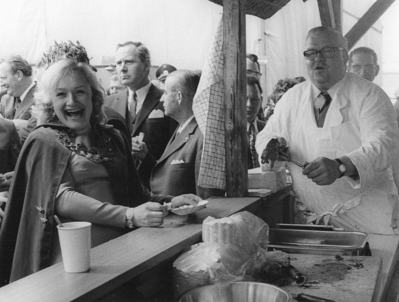 Hermann Ilchmann im weißen Kittel an seinem Grillstand, davor eine lachende Besucherin mit Krone